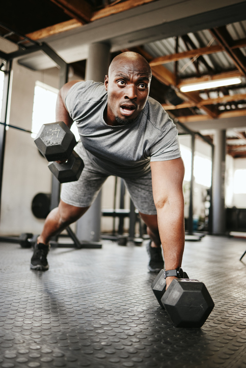 Fitness, gym and black man doing a workout with weights for strength, wellness and training. Motivation, sports and strong African athlete doing push up exercise in a sport, health and active studio.